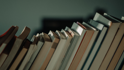 A stack of books are leaned to the right before a blurry grey backdrop.