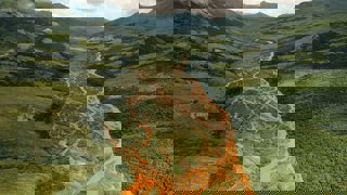 An orange coloured river, which is nearly dried out, meandering through lush green mountains and hills.