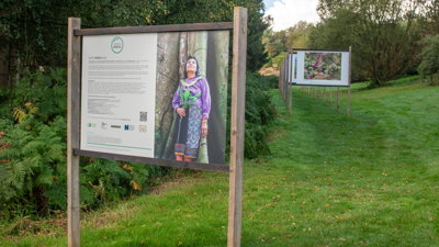Wooden sign in a field of grass with a text about the Earth Photo 2023 exibition on the left and one of the winning images to the right.