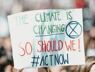 Climate action protest sign reading 'the climate is changing, so should we! Act now'.