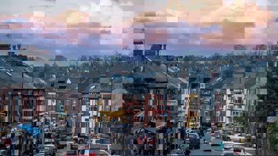 Row of houses along a busy road with parked cars.
