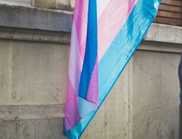 Person holding trans flag behind them.