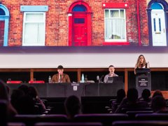Three people at annual conference with one person giving a keynote speech