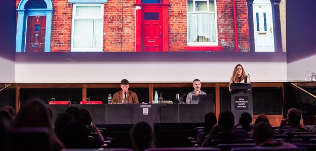 Three people at annual conference with one person giving a keynote speech