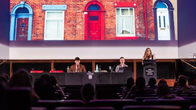 Three people at annual conference with one person giving a keynote speech