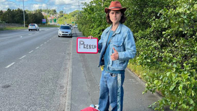 Person standing by the side a road, holding a sign. 