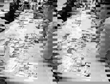 People sitting around a table looking at postcards and drawing