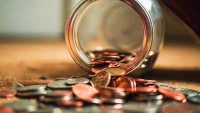Copper and sliver coins spill out of a tipped over glass jar. this sits upon a carpeted surface
