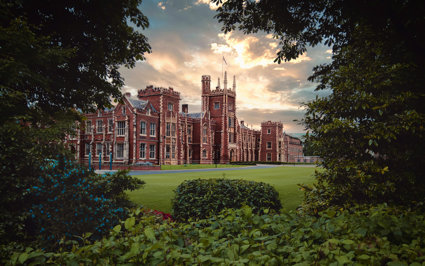 Red brick university building with grass at the front, surrounded by trees