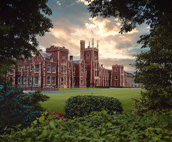 Red brick university building with grass at the front, surrounded by trees