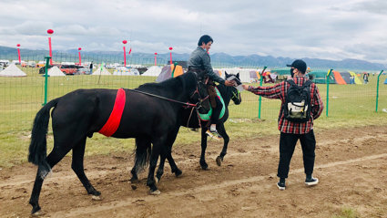 A rider on horseback, leading a second horse adorned with a red sash, receives a letter from a person standing on the ground.