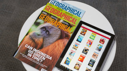 A pile of three print copies of Geographical magazine next to a tablet that displays covers of magazines in the Geographical magazine app.