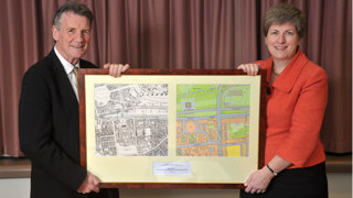 A woman and man each holding up one side of an old and a framed map.