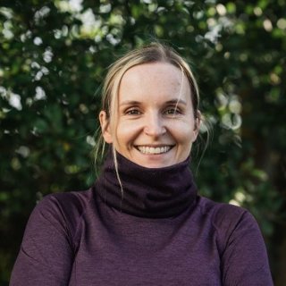 Cat Burford wearing purple turtleneck against background of trees. 