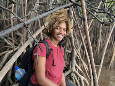 Woman in red t-shirt and wearing a backpack sitting at the edge of mangroves.