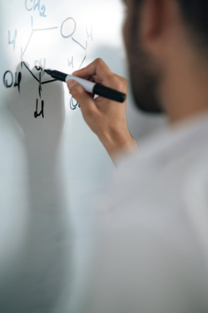 A person writing scientific workings on a white board
