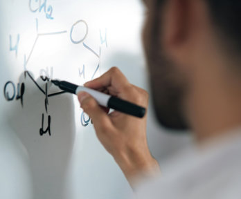 A person writing scientific workings on a white board