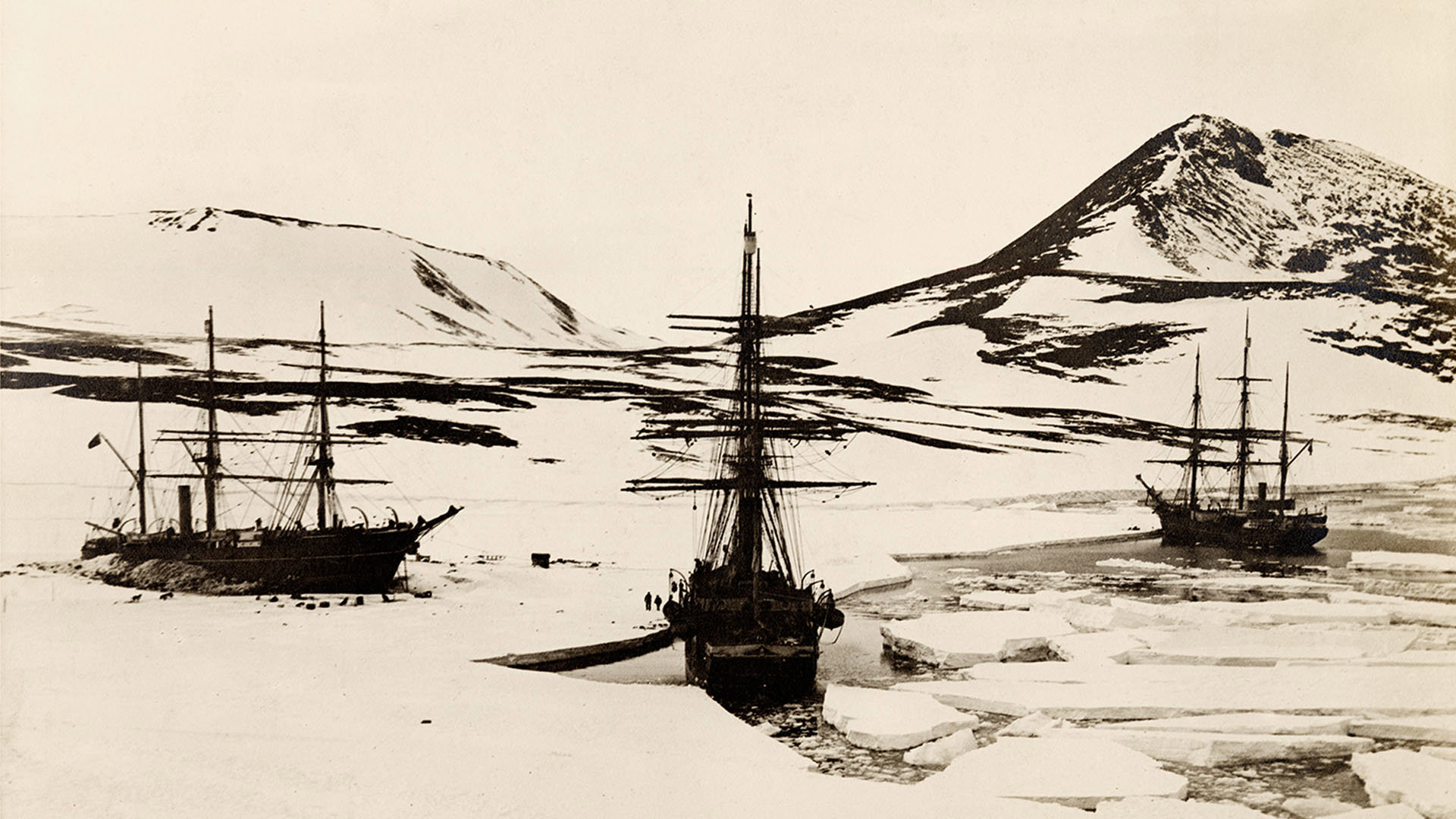 Old black and white photograph of three ships stuck in ice.