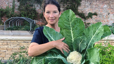 Rachel de Thame standing in a garden showing a cauliflower. 
