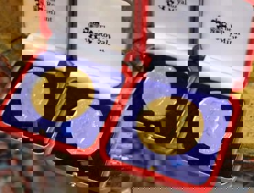 Two gold medals shown in open red boxes with blue velvet, the words 'The Royal Mint' are written on each box