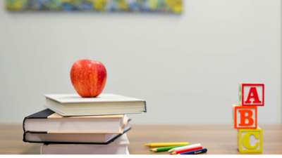 A an apple on top of a stack of books, five colouring pencils and alphabet blocks sit on top of a wooden table.