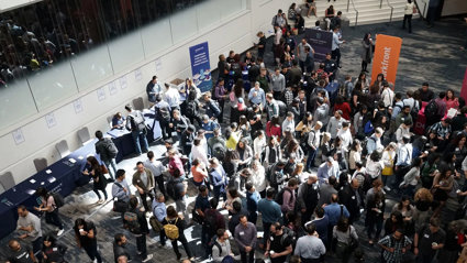 Conference hall with people chatting and gathering around stalls.