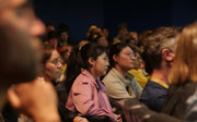 Two people in an audience look pensively while they listen