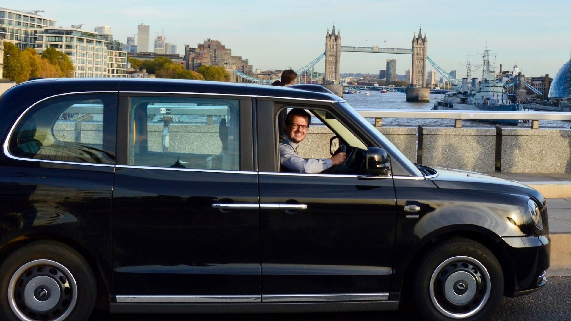 A person driving a black cab over London Bridge.
