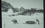 Black and white photograph of people pushing a sledge through snow.