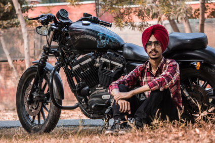 A man in a red turban sitting up against a Harley Davidson motorbike