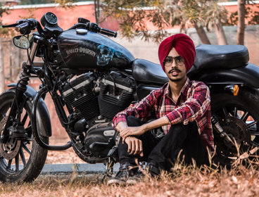 A man in a red turban sitting up against a Harley Davidson motorbike