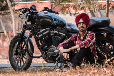A man in a red turban sitting up against a Harley Davidson motorbike
