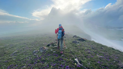 Person walking along a rocky cliff path on a foggy day.