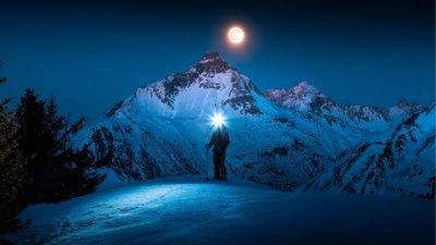 Mountain scape at night with full moon and someone skiing.