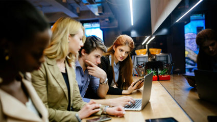 A group of people crowded around a laptop looking at the screen.