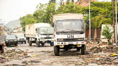 UN trucks driving on a dirty street full of litter.