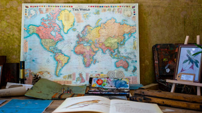 Map of the world poster with a book, paints and easel on the table in front.