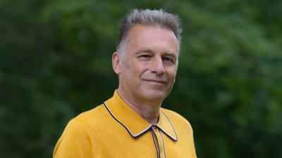 Headshot of Chris Packham wearing a bright yellow polo against a green, blurred out background.