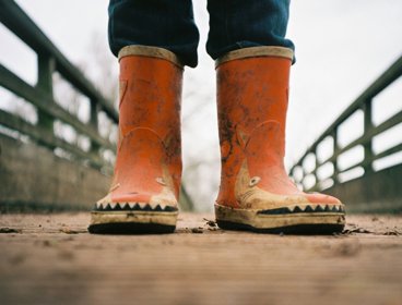 Pair of red childrens rain boots on a muddy path.