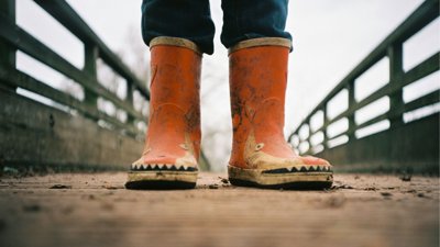 Pair of red childrens rain boots on a muddy path.