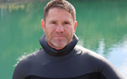Steve Backshall facing the camera standing next to a body of water