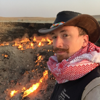 Spike Reid wearing a cowboyhat and scarf standing next to a crater with burning lava.
