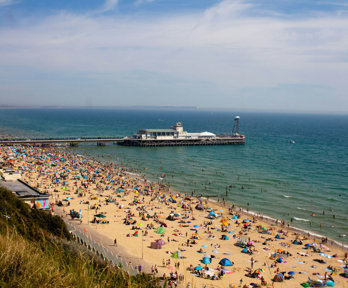 A view over a beach packed with people with a pier jutting out into the sea