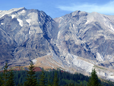 Mount St Helens with blue sky and trees in the foreground.