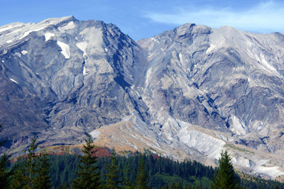 Mount St Helens with blue sky and trees in the foreground.