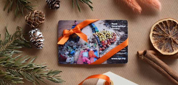 A membership card wrapped up in orange ribbon on brown wrapping paper with festive foliage surrounding it, including acorns, holly and cinnamon sticks.