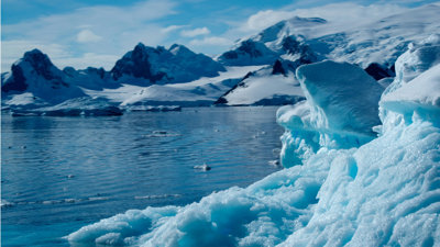 A large, floating iceberg surrounded by snow-covered mountains.