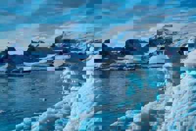A large, floating iceberg surrounded by snow-covered mountains.