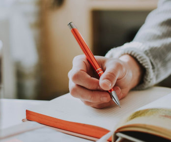 Person holding a pen and writing in an open notebook on a table.