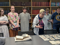 Six people standing up around a table and observing some Collections items.